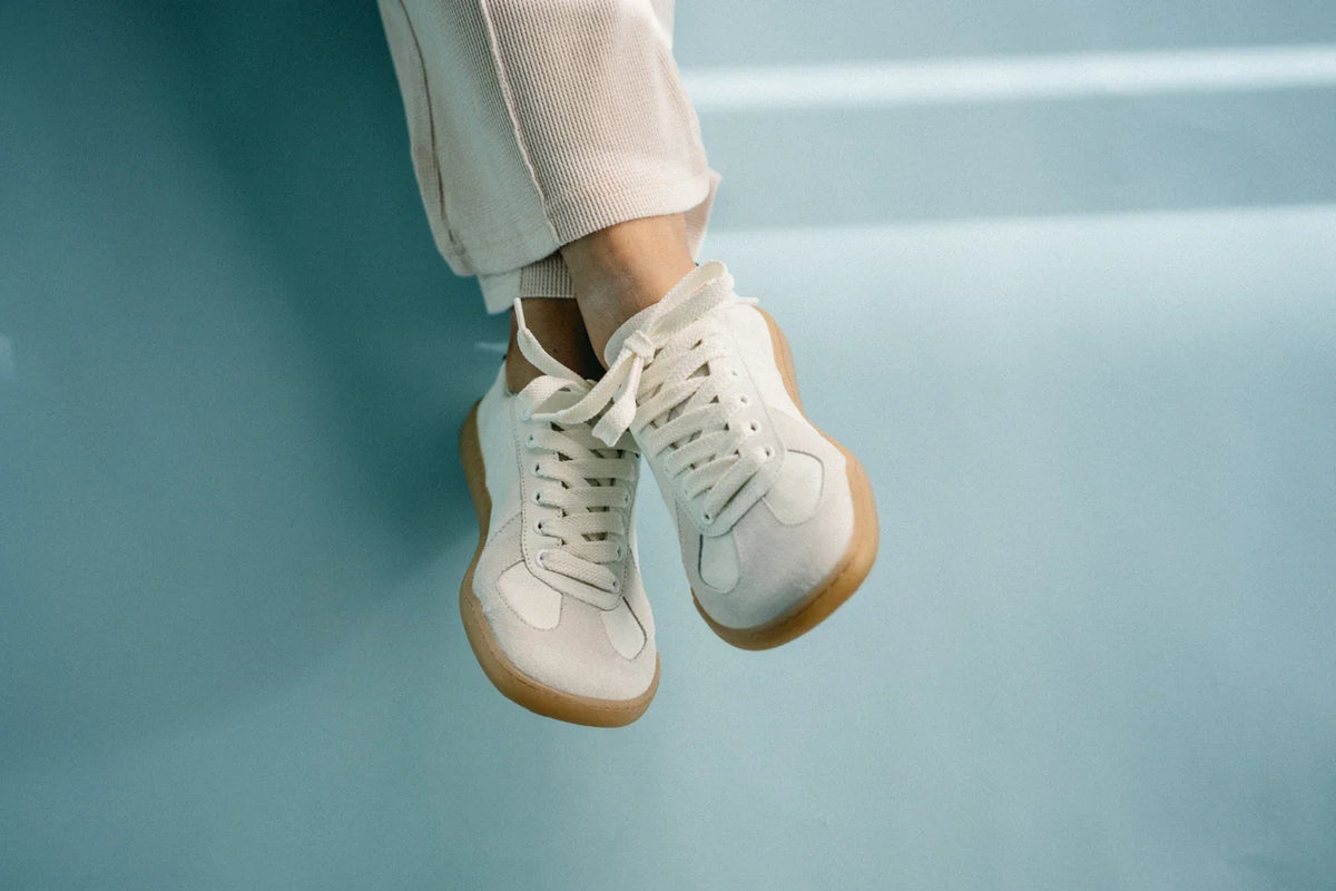 Detailaufnahme von Füßen in einer beigefarbenen Cordhose, die die weißen Barfuß-Sneaker Modell BLSN-200W White von Blusun aus Glatt- und Veloursleder mit flexibler TPU-Sohle tragen.